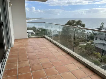 A terracotta tiled balcony behind a glass balustrade, looking out to the sea