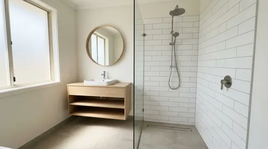 A bright bathroom with a walk in shower, white subway tiles, a round mirror and a timber vanity