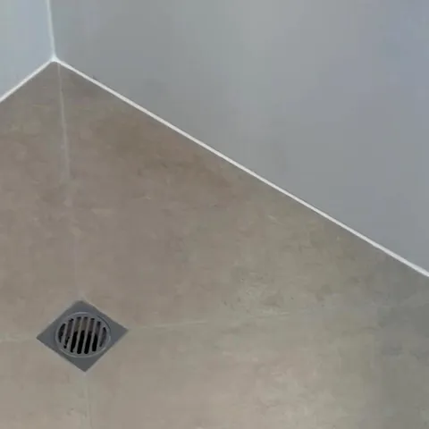The same shower floor after: clean pale grout lines and fresh white silicone along the base of the wall