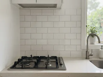 A white subway tile kitchen splashback behind a gas cooktop
