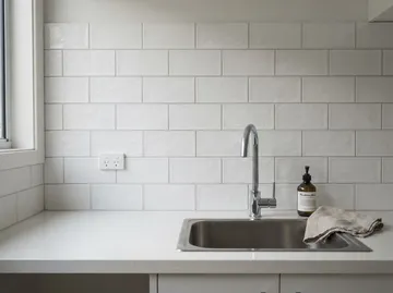 A white tiled laundry splashback above a steel sink